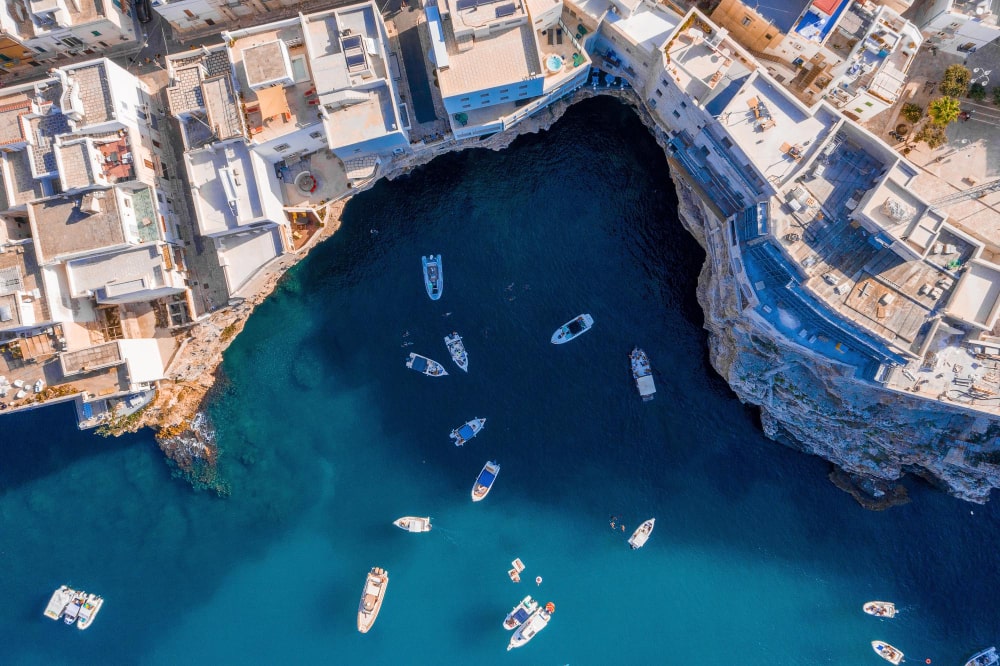 aerial-drone-photo-luxury-sail-boats-yachts-docked-near-paradise-cliff-shore-with-turquoise-clear-water-beach-min